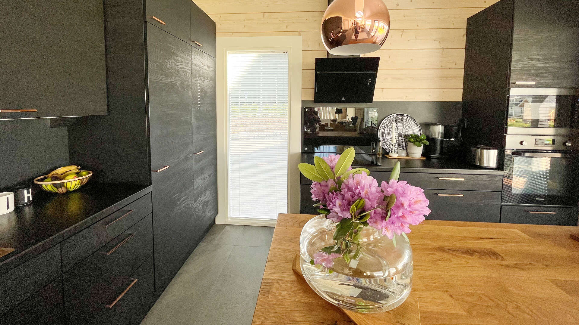 Picture of the kitchen along two walls. Black cupboard doors and furniture frames create contrast while the island in the middle creates more space for cooking. 