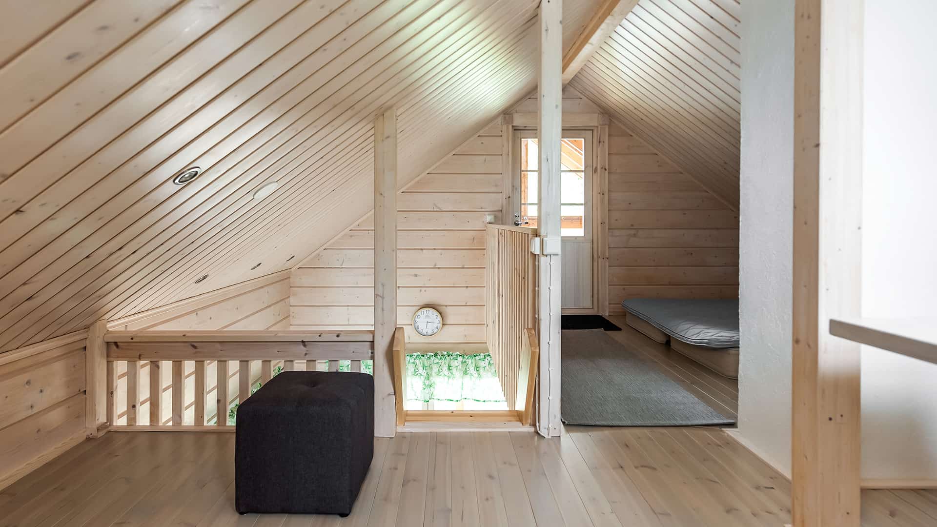 There are sleeping spots on the loft underneath the ridged roof. The log walls and ceiling panels are painted a translucent white.