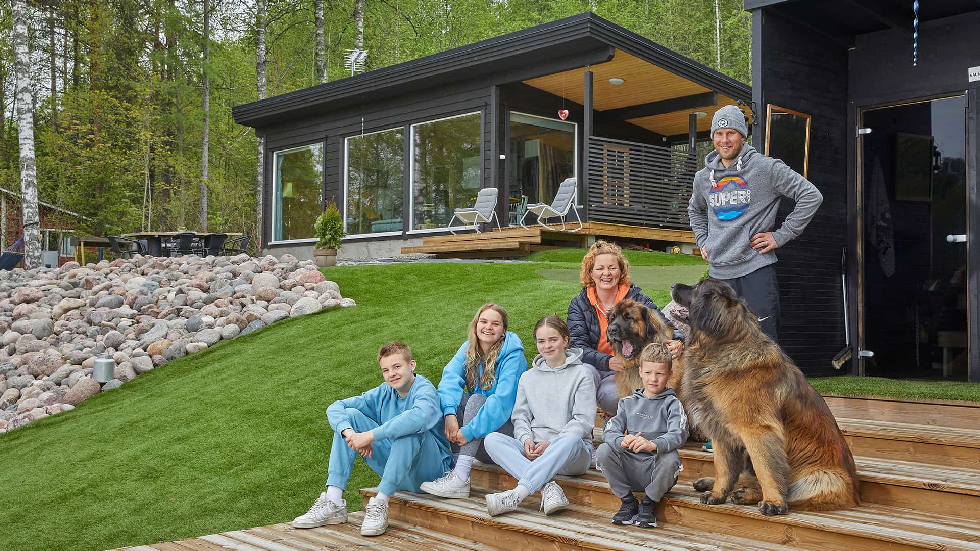 The family on the terrace of the sauna building. The background shows their modern pent-roof log cabin.