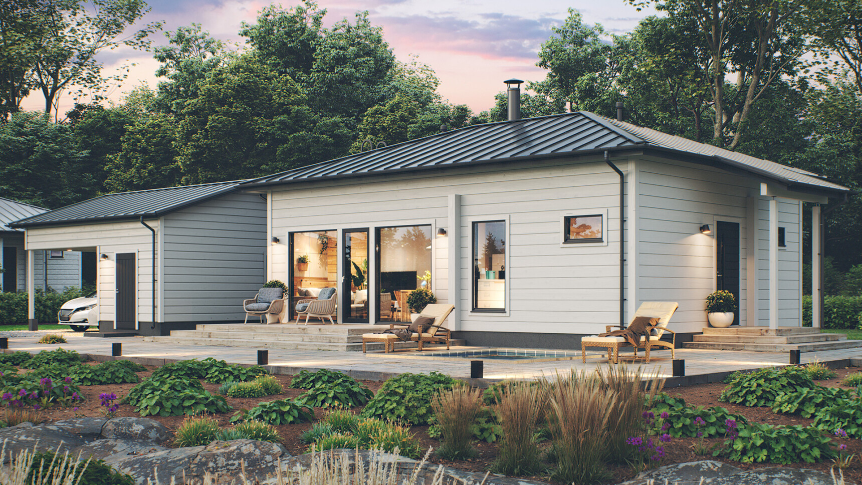 Aumakattoinen valkoinen pieni hirsitalo, jonka oleskelutilan isoista ikkunoista loistaa valot ulos.