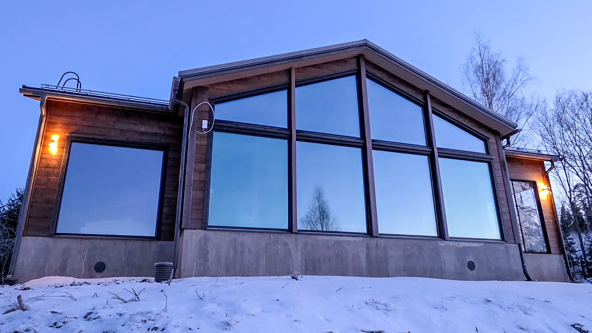 Hirsitalon takaosa isoine ikkunoineen talvisena iltana.